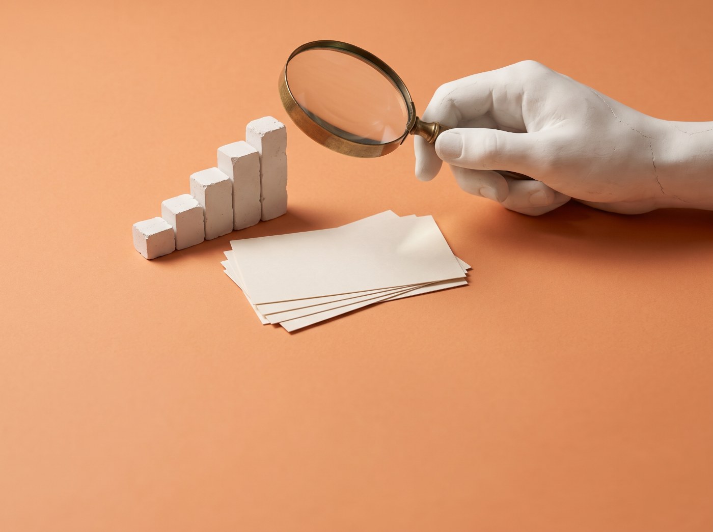 Keyword research and SEO reporting: plaster hand holding a magnifying glass over index cards and a rising bar chart